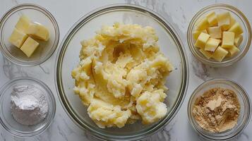A bowl of mashed potatoes surrounded by ingredients for a recipe. photo