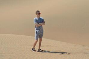 A man in a desert. A young man wearing red sunglasses standing at the sand barchan background. Dune in Maspalomas, Gran Canaria photo