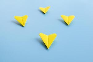 Straight view of yellow paper airplane origami leading other yellow airplanes on blue background with customizable space for text. Business and Leadership skills concept photo