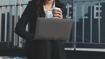 A woman in a business suit holding a coffee cup and using a laptop video