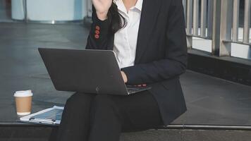 A woman in a business suit sitting on a step with a laptop video