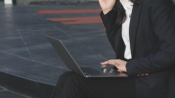 A woman in a business suit sitting on a step with a laptop video
