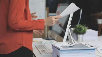 A woman is holding a piece of paper while standing in front of a computer video