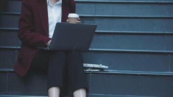 A woman in business attire sitting on some steps with a laptop video