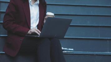 A woman in a business suit sitting on steps with a laptop video