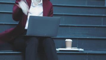 A woman in a business suit sitting on some steps with a laptop video