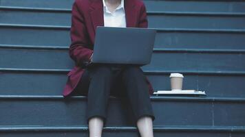 A woman in a business suit sitting on the steps with her laptop video