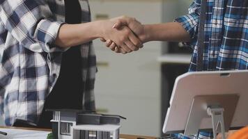 Two people shaking hands over a desk with a computer video