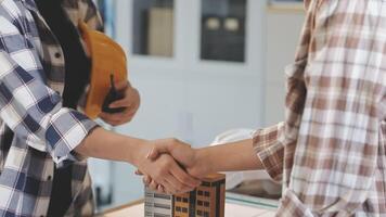 Two people shaking hands over a table with a model house video