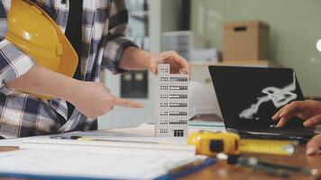 A man in a hard hat and helmet is pointing at a model of a building video