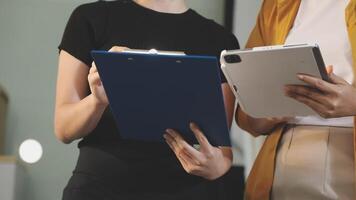 Two women holding a clipboard and looking at a tablet video