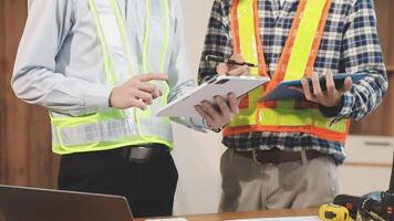 Two construction workers are standing in front of a desk video