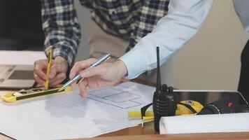 Two people working on blueprints with a laptop video
