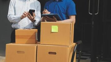 Two men standing near boxes and a phone video