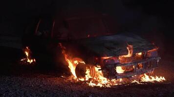A vehicle is burning fiercely during the night, creating a dramatic and dangerous scene, video