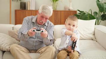 Happy family. Old senior man grandfather boy grandson playing game with joysticks at home. Smiling grandparent and child using gamepads for game. Older generation modern tech usage video
