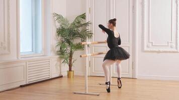 Young ballerina in tutu skirt stretching practicing ballet positions dancing near ballet barre in dance class. Young classical dancer woman in dance studio. Ballet class training Ballet school concept video