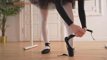 Ballerina puts on pointe shoes on leg in dance class. Classical ballet dancer woman in dance studio. Ballerina putting on tying classical pointe shoes for dance training. Ballet school concept video
