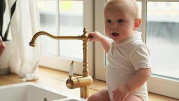 Happy family at home. Cute little baby toddler child sitting on table in kitchen at home. Newborn baby relax playing having fun indoor. Love care concept. Infant baby resting at home. Happy child video
