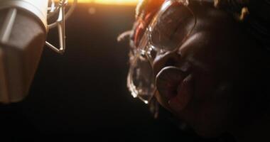 A person with glasses and a microphone in front of a light video