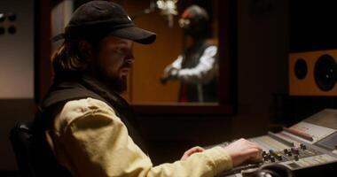 A man in a hat and jacket sitting at a mixing desk video