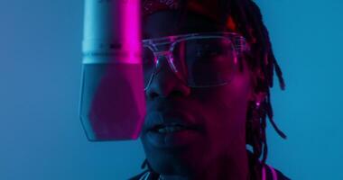 A man with glasses and a microphone in front of a blue light video