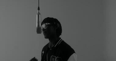 A man in a black jacket and sunglasses is standing in front of a microphone video