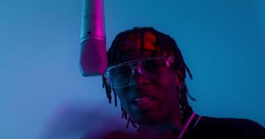A man with dreadlocks and glasses in front of a microphone video