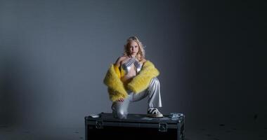 A woman in a yellow fur coat sitting on top of a suitcase video