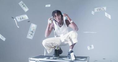 A man sitting on top of a suitcase with money falling from the sky video