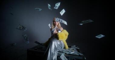 A woman in a silver dress sitting on a suitcase with money falling from the sky video