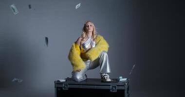A woman in a silver suit sitting on a suitcase with money falling from the sky video