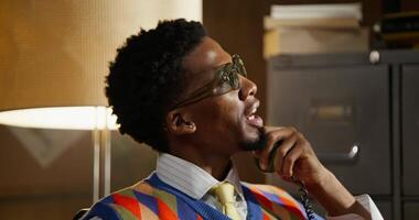 A man in a colorful sweater and tie talking on the phone video
