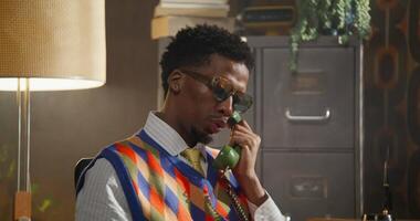 A man in a colorful sweater and tie talking on the phone video