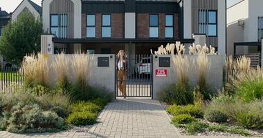 A woman is standing in front of a gate in front of a house video