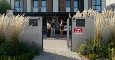 A couple standing in front of a house with a sign that says for sale video