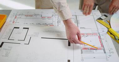 A man is holding a pencil and pointing at a blueprint video