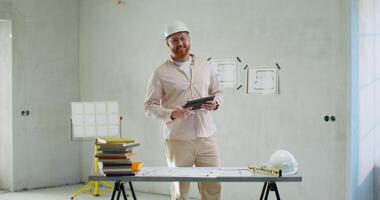 A man in a hard hat standing in front of a table with a tablet video