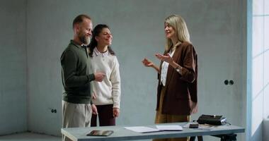 Three people standing around a table talking video