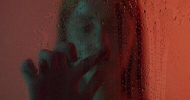 A woman is standing in front of a window with water drops on it video