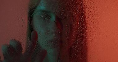 A woman is looking through a window with water drops on it video
