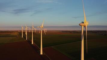 A lot of rotating wind turbines against the background of multi-colored fields. Drone footage, wind farm view at sunset video
