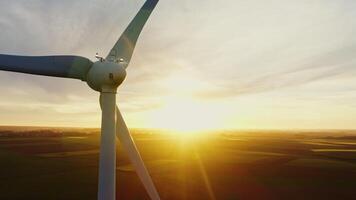 Close-up of the rotating blades of a wind turbine, from the back of the turbine against the backdrop of the setting sun. Wind farm at sunset from a drone video