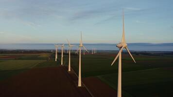Horizontal panning from a drone, a view of a massive wind farm among bright green fields. footage of a drone at the level of the rotating blades of a wind turbine in the evening video