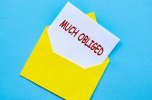 Yellow envelope on a blue cover with a white card partially pulled out with Much Obliged text photo