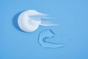 A smear of white cream And a drop of serum on a blue background. photo