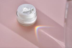 An open jar of cream with its texture on a pink background. photo