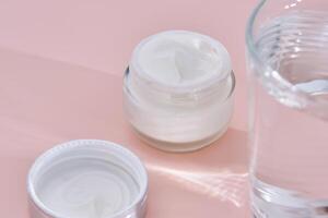 An open jar of cream with its texture on a pink background. photo