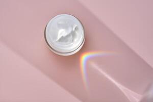 An open jar of cream with its texture on a pink background. photo
