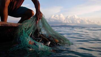 fisherman pulling up his net filled with fish at sunset photo